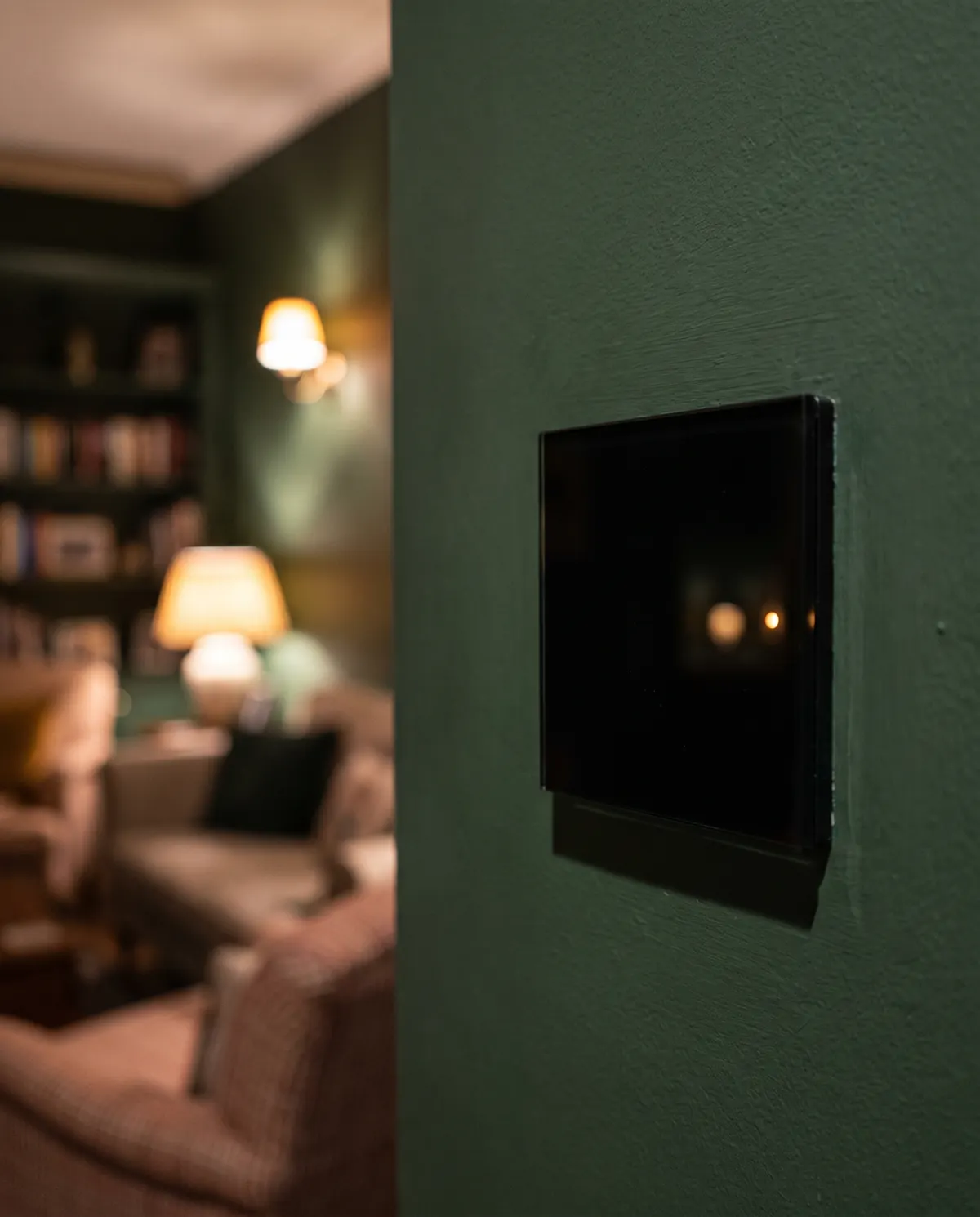 Black glass smart switch on a dark green wall